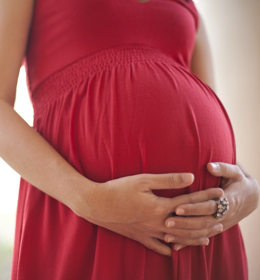 A pregnant woman resting her hands on her belly.